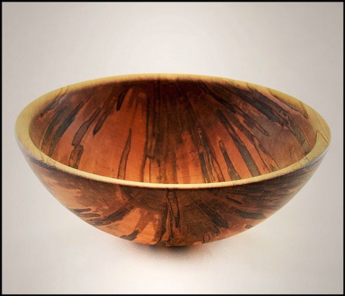 Left Turn wood artist David Yeatts creates unique functional wooden bowls. He began wood turning in 1987 after a career in the food industry.  Turning bowls captured his imagination and he has developed a distinctive shape and feel for his bowls. Each beautiful bowl is turned from Ambrosia Maple. Ambrosia Maple takes its name from the pest – the Ambrosia Beetle. All of his bowls are made from trees that have naturally fallen as a result of this pest. This beetle burrows into the wood, killing the tree, and leaving behind the interesting striations amongst the grain of the wood. The marks from the beetle are a distinctive characteristic of his bowls.
<br><br>
He works from his home studio in Vinton, VA where he has taught his son to turn as well.